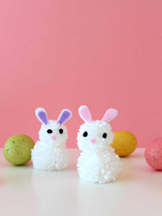 Set of pom pom bunnies with Easter eggs against pink background